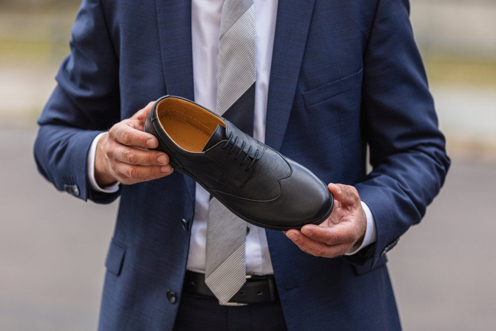 Ein Paar Oxford-Schuhe aus schwarzem Leder BRIQ Prime von ZAQQ mit Schnürung, bei der ein Schuh auf dem anderen vor einem weißen Hintergrund ruht. Diese eleganten Business-Schuhe strahlen Raffinesse aus und sind mit einer bequemen Barfußsohle für ganztägiges Tragen ausgestattet.