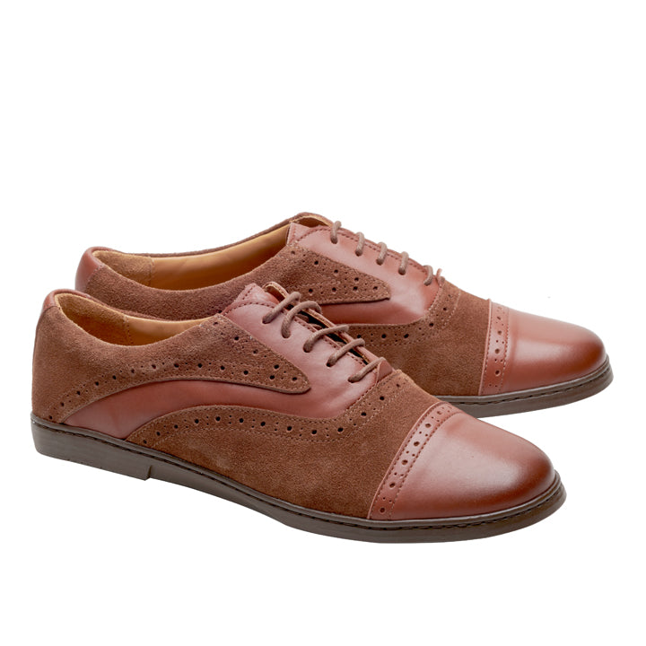 Wir präsentieren die ZAQQ QENTLE Cognac-Schuhe, eine exquisite Mischung aus braunem Leder und Wildleder im Flügelkappendesign mit Schnürverschluss. Diese aus hochwertigem Nappaleder gefertigten Schuhe sind mit eleganten perforierten Details verziert und haben einen niedrigen Absatz, der sich auf einem schlichten weißen Hintergrund abhebt.