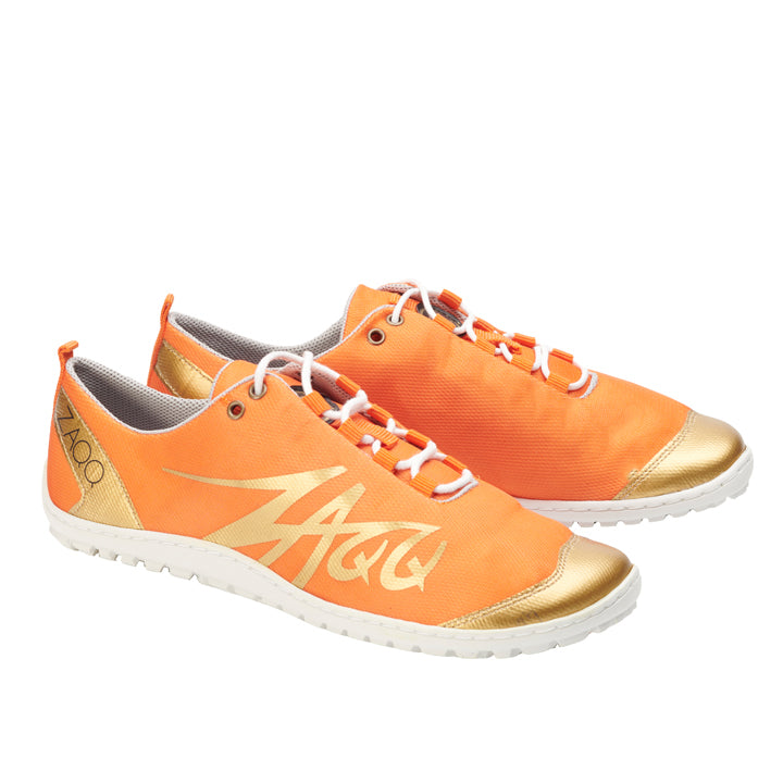 Erleben Sie unübertroffenen Tragekomfort mit den SQIM Orange Gold Sportschuhen von ZAQQ. Diese Schuhe wurden als Barfußschuh für ein natürliches Tragegefühl entworfen und verfügen über orangefarbene Oberteile, ergänzt durch weiße Sohlen und Schnürsenkel sowie goldene Akzente an den Zehen. Das stilisierte ZAQQ-Logo an den Seiten unterstreicht die Verwendung von hochwertigem Recyclingmaterial.