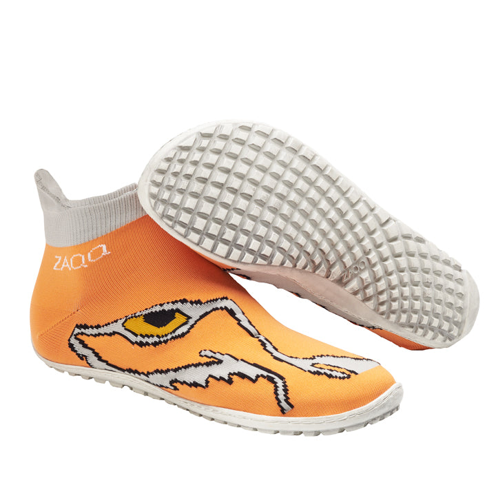 Ein Paar SOQQ Eye Orange von ZAQQ zeigt ein lebendiges Tigergesichtsdesign und verspricht hervorragenden Tragekomfort. Die Schuhe haben weiße Sohlen mit strukturierten Griffen. Ein Schuh steht aufrecht, während der andere mit der Sohle nach oben platziert ist, um das komplizierte Muster hervorzuheben.