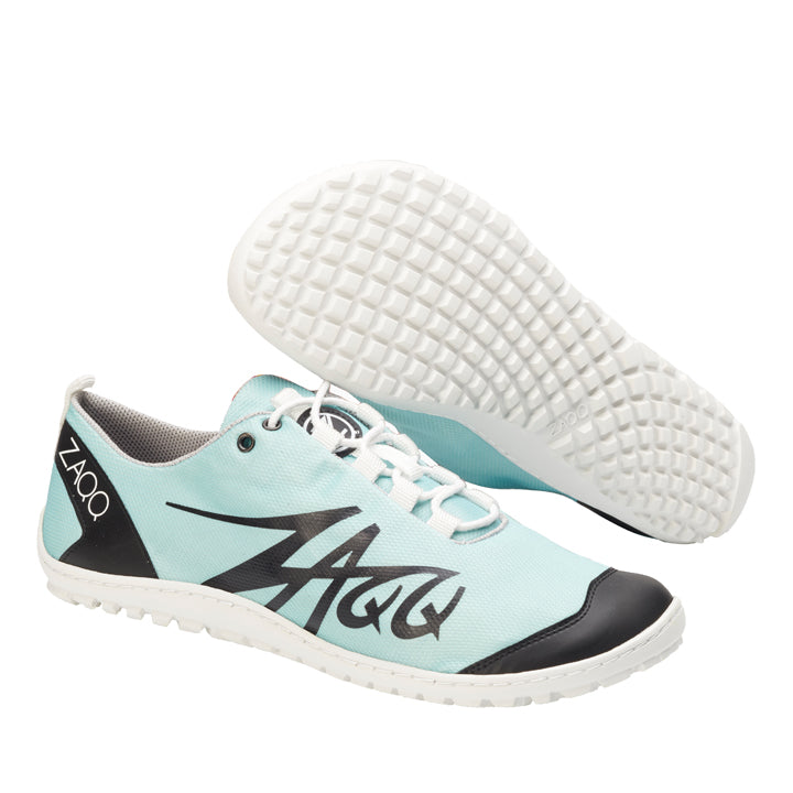 Die SQIM Turquoise Sportschuhe von ZAQQ sind aus veganem Recyclingstoff in Hellblau gefertigt und verfügen über weiße Sohlen und schwarze Akzente. Der stilisierte Name der Marke ist elegant an der Seite angebracht. Ein Schuh steht aufrecht, während der andere geneigt ist, um das komplizierte Profilmuster auf seiner Sohle zu präsentieren.