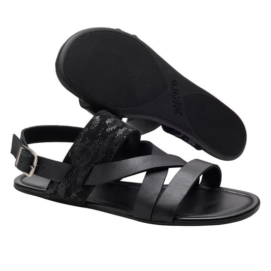 Die flachen Sandalen ZAQQ PERLAQ Black sind mit Riemen aus Nappaleder in glatter oder strukturierter Ausführung ausgestattet und verfügen über einen Schnallenverschluss. Eine Sandale liegt elegant auf der Seite, um die Sohle hervorzuheben.