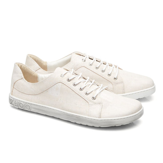 Die QORE Low Vegan White Sneaker von ZAQQ sind cremefarben mit weißen Schnürsenkeln und Sohlen. Diese Schuhe zeichnen sich durch ein minimalistisches Design mit einem subtilen geometrischen Muster auf dem Körper aus und zeigen das Logo der Marke auf der Ferse. Sie werden vor einem schlichten weißen Hintergrund präsentiert.