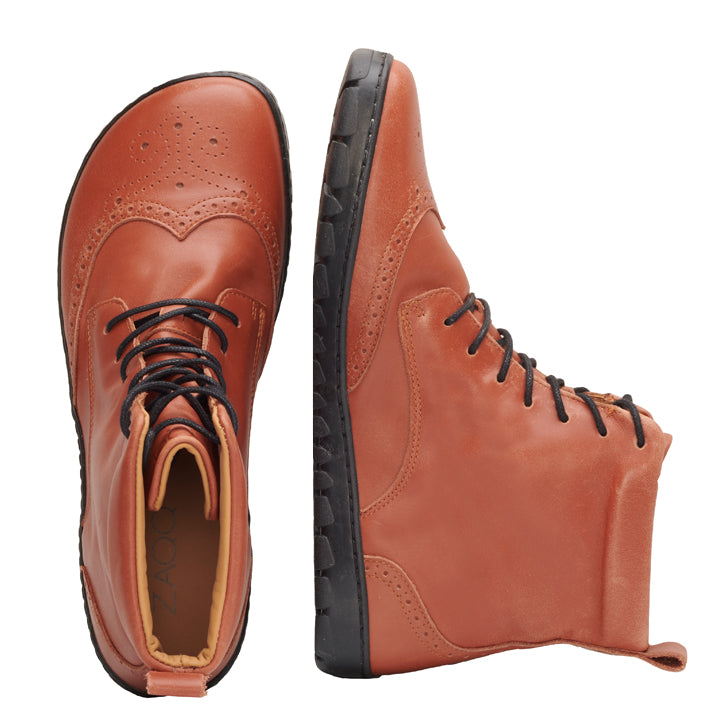 Die QUINTIC Brogue Cognac Lederstiefel von ZAQQ sind in Braun mit aufwendigen Brogue-Details abgebildet und werden aus zwei Winkeln gezeigt: einmal aufrecht und einmal auf der Seite liegend, wodurch die robuste schwarze Sohle hervorgehoben wird.