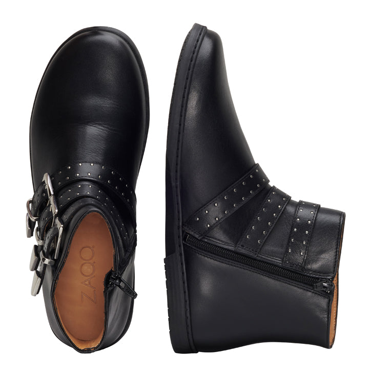 Zwei schwarze QLANCE Black Silver Plain Stiefeletten von ZAQQ sind von oben und von der Seite zu sehen. Der rechte Stiefel ist mit silbernen Schnallen und kleinen Nieten verziert. Beide Stiefel haben Reißverschlüsse und eine flache Sohle. Die Innensohle besteht aus hochwertigem Nappaleder und trägt in eleganter Schrift den Markennamen QLANCE.