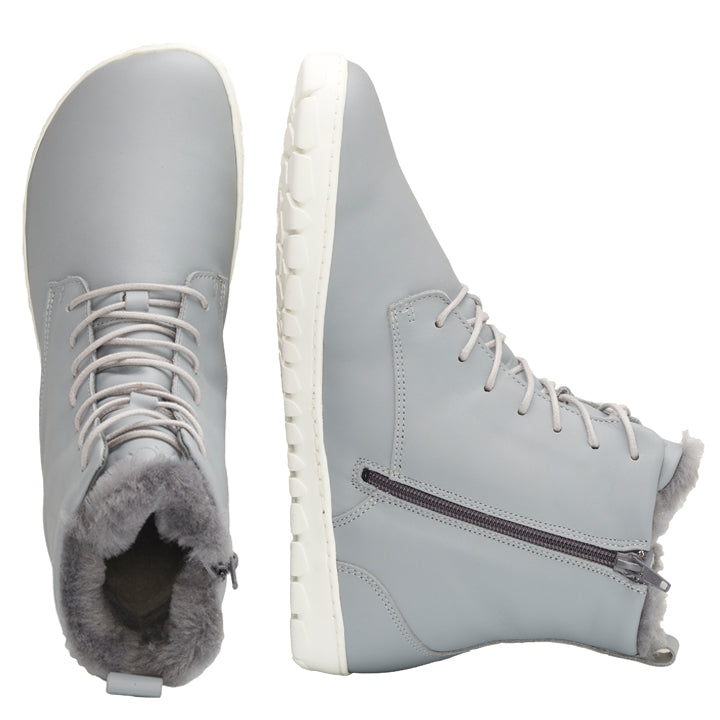 Wir präsentieren den QUINTIC Winter Blue Grey, ein stilvolles Paar High-Top-Stiefel von ZAQQ. Diese Winterstiefel zeigen einen raffinierten Grauton, ergänzt durch weiße Sohlen und praktische seitliche Reißverschlüsse. Das Design zeichnet sich durch elegante graue Schnürsenkel aus und ist für zusätzlichen Komfort mit warmem, kuscheligem Fell gefüttert. Ein Stiefel ist wunderschön von oben zu sehen, während der andere von der Seite aufgenommen wurde, alles vor einem makellos weißen Hintergrund.