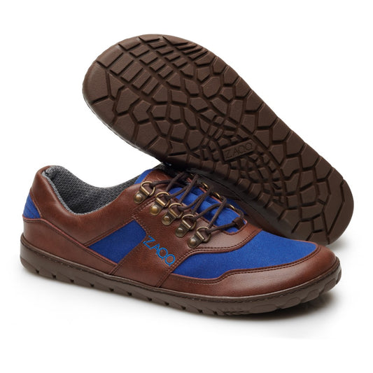 Wir präsentieren den HIQE Low Brown Blue Waterproof von ZAQQ: Ein Paar Freizeitschuhe für Herren aus veganem Material. Diese Schuhe zeichnen sich durch braunes Leder und blaue Stoffakzente aus. Ein Schuh hebt die Profilsohle mit einem sechseckigen Muster hervor, während der andere eine Seitenansicht mit Metallösen und blauen Schnürsenkeln bietet.