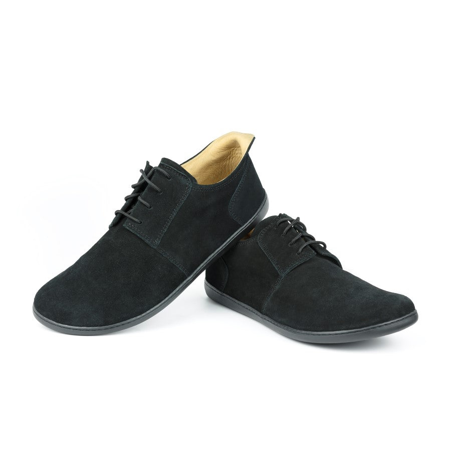 Ein Paar PIQUANT Velours Black Schuhe von ZAQQ zeichnet sich durch ein minimalistisches Design mit Schnürsenkeln aus. Ein Schuh steht aufrecht, während der andere lässig auf einem schlichten weißen Hintergrund lehnt und das glatte schwarze Veloursledermaterial zur Geltung bringt.