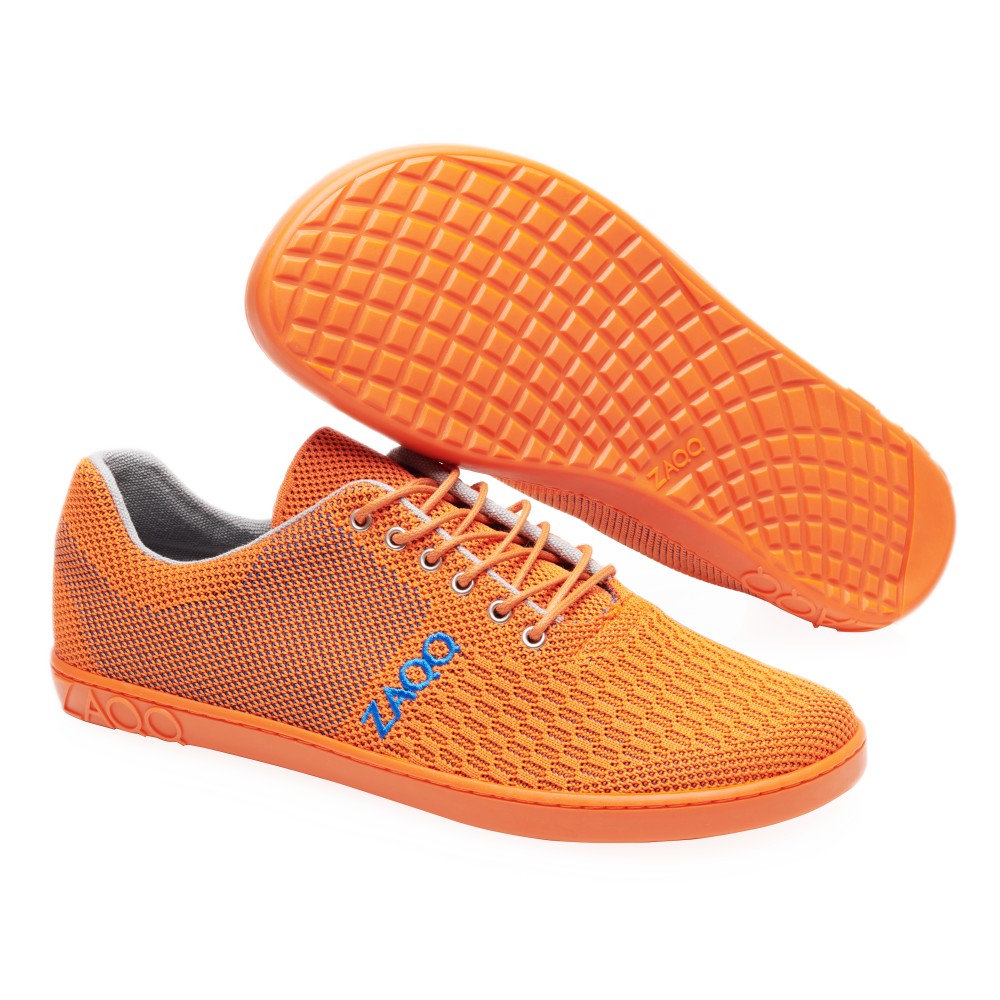 Die leuchtend orangefarbenen Mesh-Sportschuhe QNIT Orange verfügen über ein Obermaterial aus veganem Strickgewebe und eine strukturierte Kautschuksohle. Ein Schuh steht aufrecht, während der andere seitlich steht und die Sohle sichtbar ist. Der Markenname ZAQQ ist seitlich in Blau abgebildet.