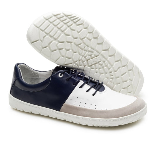 Gezeigt werden zwei stylische Low-Top-Barfuß-Sneaker aus der QOOL Navy-Linie von ZAQQ. Ein Schuh zeigt die Seiten- und Vorderansicht und verfügt über ein Farbschema in Marineblau, Weiß und Beige mit Perforationen für zusätzlichen Tragekomfort, während der andere seine strukturierte weiße Sohle offenbart.