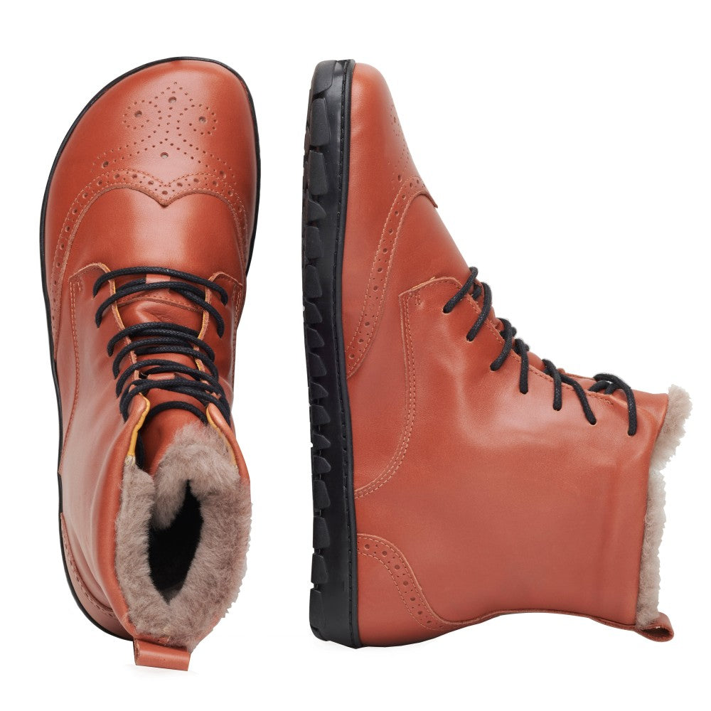 Ein Paar QUINTIC Winter Brogue Cognac-Stiefel von ZAQQ wird aus zwei Blickwinkeln präsentiert. Der linke Stiefel zeichnet sich durch aufwendige Perforationen und ein kuscheliges Lammfell-Futter aus, während der rechte Stiefel seine schwarze, robuste Sohle und das Schnürdesign hervorhebt.