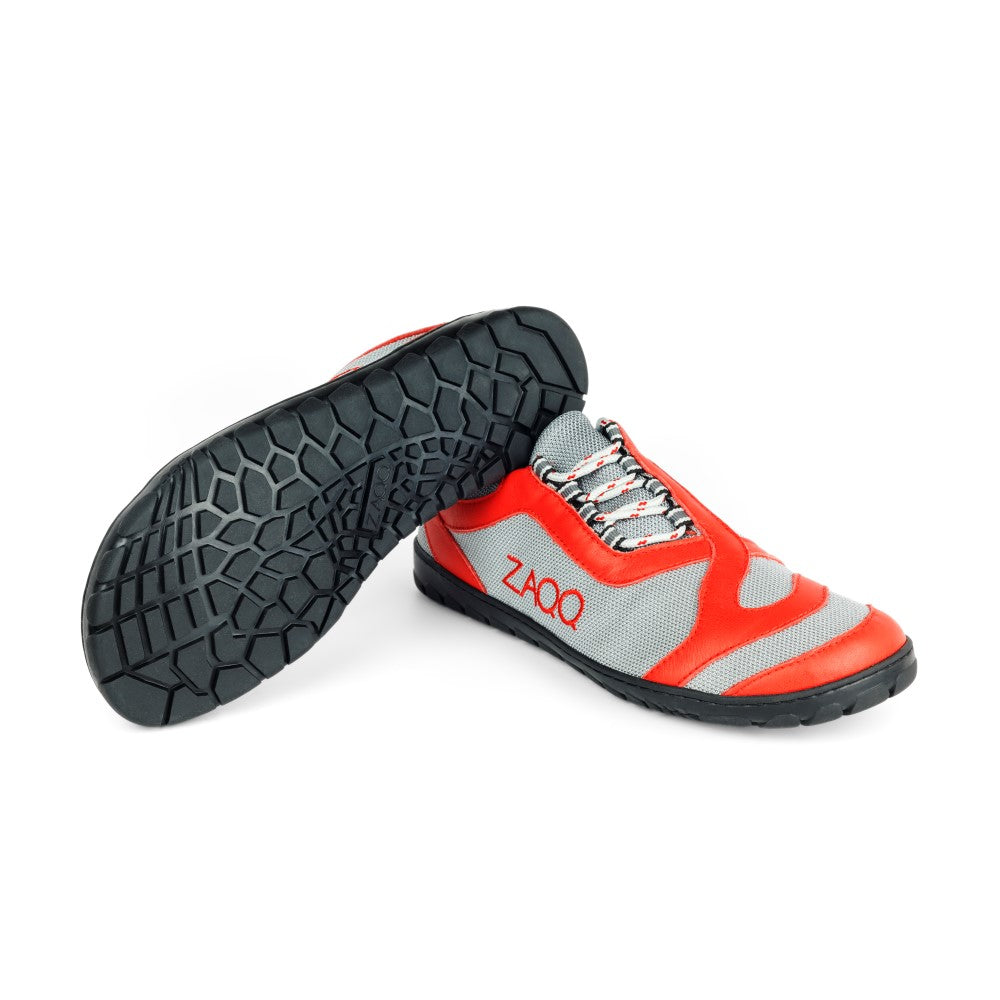 Ein Paar ZAQQ QUIQ Trail Lightred Sportschuhe in Rot und Grau mit schwarzer Sohle. Das Logo steht auf einem Schuh aufrecht und auf dem anderen diagonal, was das atmungsaktive Sohlenmuster hervorhebt.