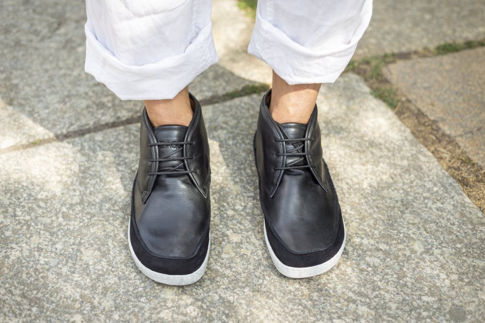 Eine Person in weißen Hosen mit Umschlag und den schwarzen Leder-Sneakers QUITMAN von ZAQQ steht auf einem Steinpflaster. Die Sneaker sind geschnürt und haben weiße Sohlen. Die Beine und Schuhe sind in der Bildmitte platziert und fangen einen lässigen Stil ein.