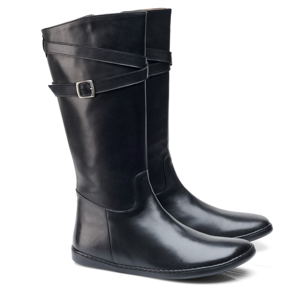 Ein Paar elegante, schwarze ATTRAQT Nappa Black Kniestiefel von ZAQQ mit abgerundeten Zehen und dekorativen Knöchelschnallen. Die Stiefel haben ein glänzendes Finish und flache Sohlen, die nebeneinander auf einem weißen Hintergrund angeordnet sind.