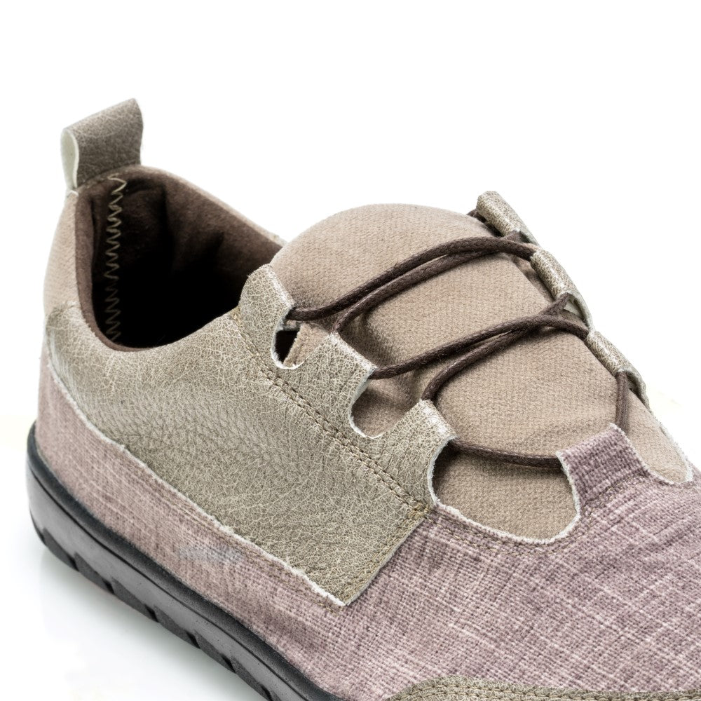 Nahaufnahme des QUEST Low Brown Waterproof Freizeitschuhs von ZAQQ mit strukturiertem Stoff und einzigartigem Schnürdesign. Dieser vegane Wanderschuh hat eine schwarze Sohle und eine Aufreißlasche an der Ferse. Seine Mischung aus Beige- und Brauntönen sorgt für ein erdiges Aussehen, ideal für jedes Abenteuer.